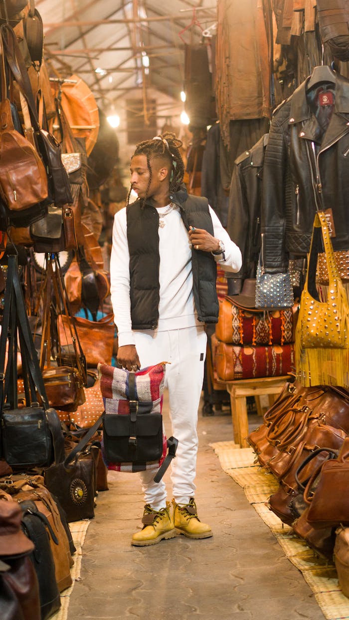 A stylish young man explores a bustling leather goods market filled with bags and jackets.
