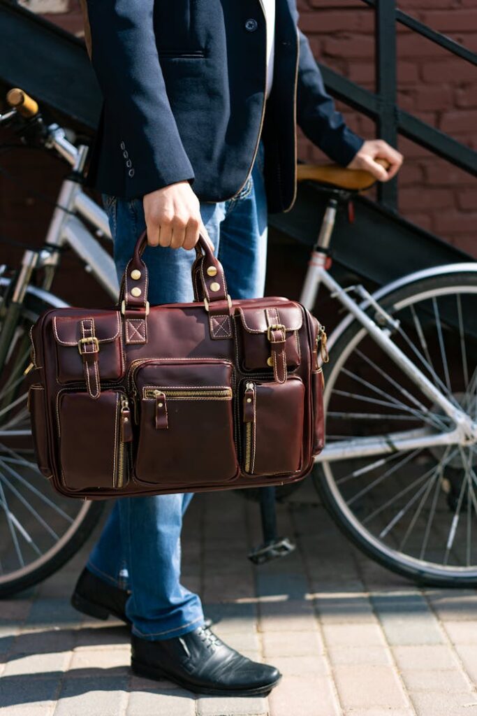 Close-up of a man in a suit holding a leather briefcase next to a bicycle outdoors.